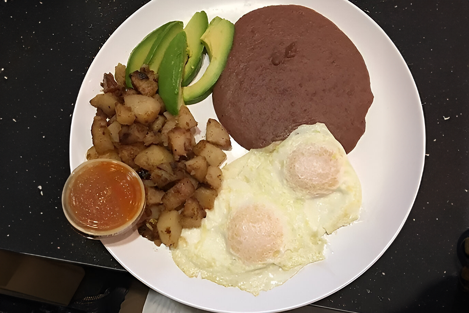 A plate of food with eggs, potatoes and avocado.