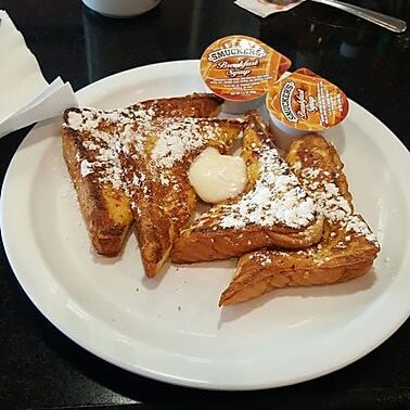 A plate of french toast with butter and powdered sugar.