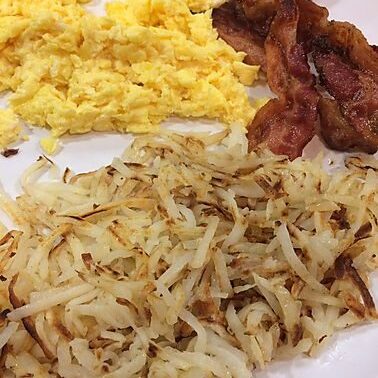 A plate of food with hash browns, eggs and bacon.